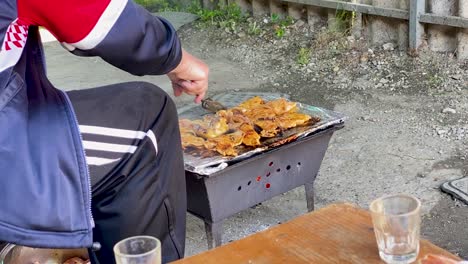 a peasant in a dirty clothes grills chicken, rural croatia