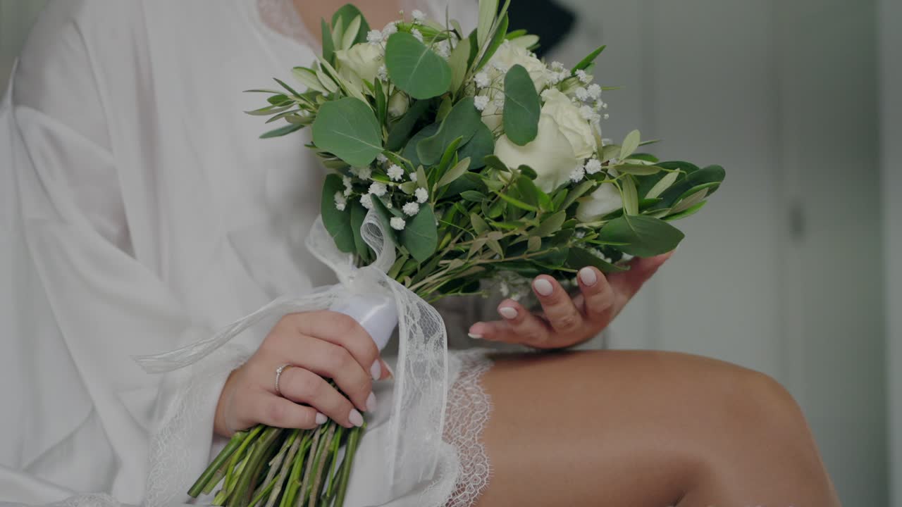 Sposa in vestaglia che tiene in mano un bouquet di fiori bianchi, catturando un momento sereno e intimo prima del matrimonio
