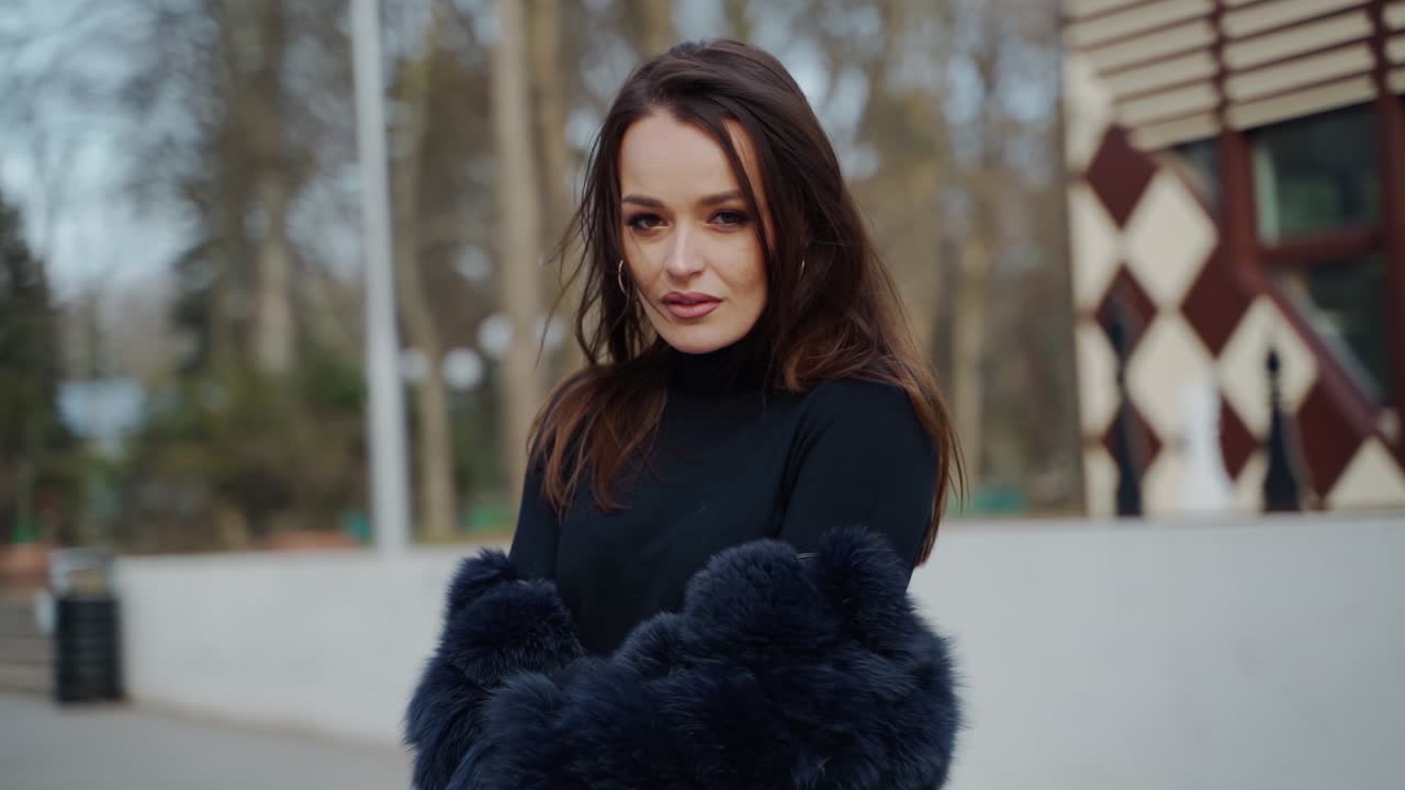 Dark-haired girl spinning around in the park. Attractive young woman in black glamour clothing posing on camera outdoors.