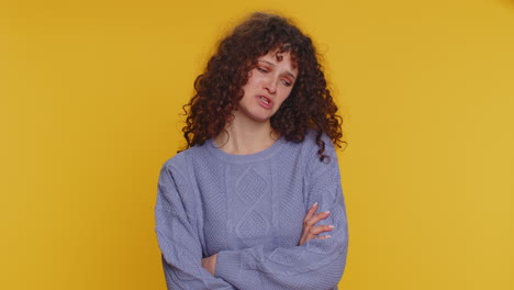 mujer con el cabello rizado y los brazos cruzados parece escéptica mientras está de pie contra un fondo amarillo