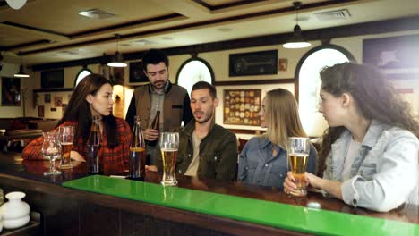 handsome bearded young man is talking to his friends and gesturing emotionally while sitting in local pub at counter. his mates are listening to him carefully.