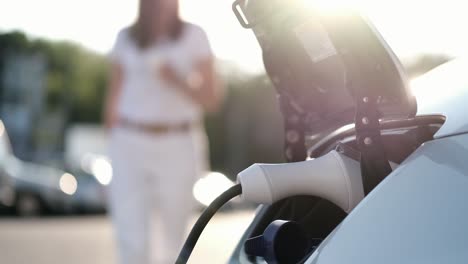 Woman-unplugging-the-charger-from-her-hybrid-car,-electric-vehicle-charging-batteries-in-a-parking-lot