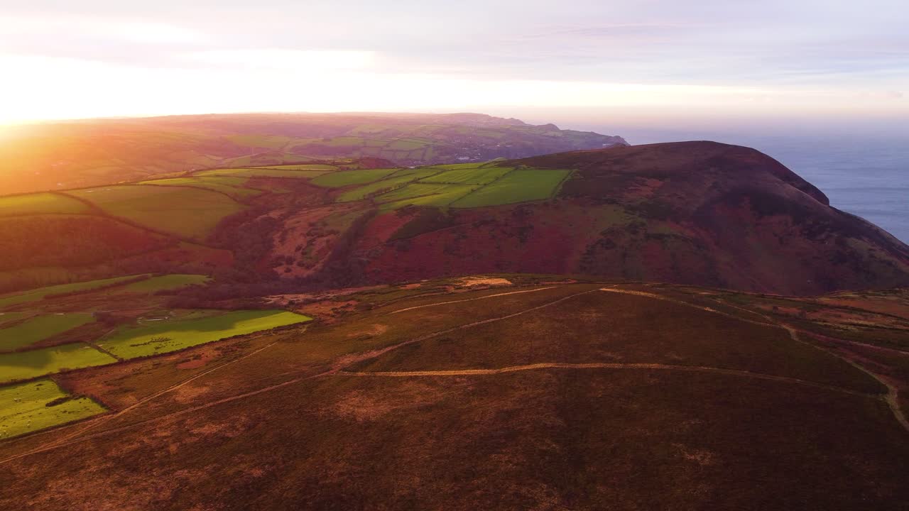 Langzame zijwaartse luchtbeelden van de ongelooflijke kustlijn van Noord-Devon met diepe valleien bij zonsondergang. Gevarieerd landelijk landschap in Groot-Brittannië. Rustige, sfeervolle clip tijdens het gouden uur in 4K
