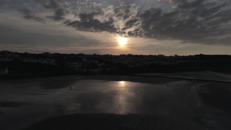 Evening-cloudy-golden-sunset-colours-across-Benllech-beach-silhouette-coastline-Anglesey-aerial-view-slow-rising-forwards