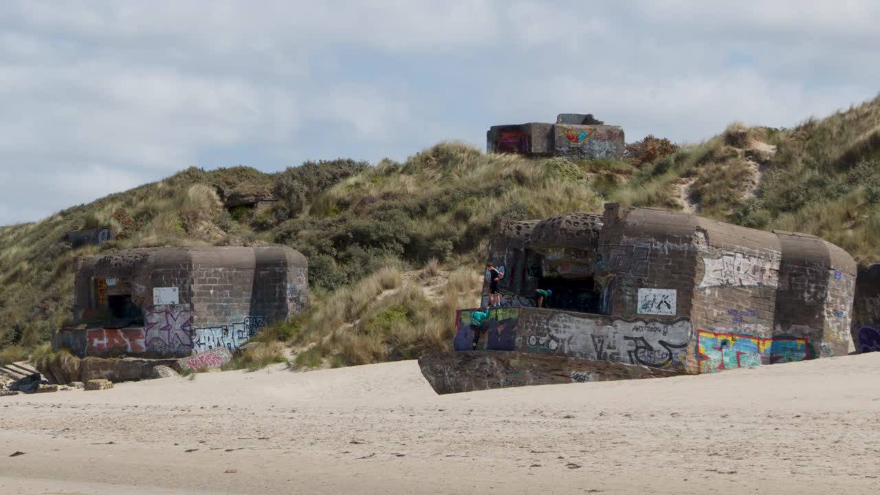 Static wide shot of colorful graffiti bunker on sandy dunes, bright daylight, calm summer atmosphere
