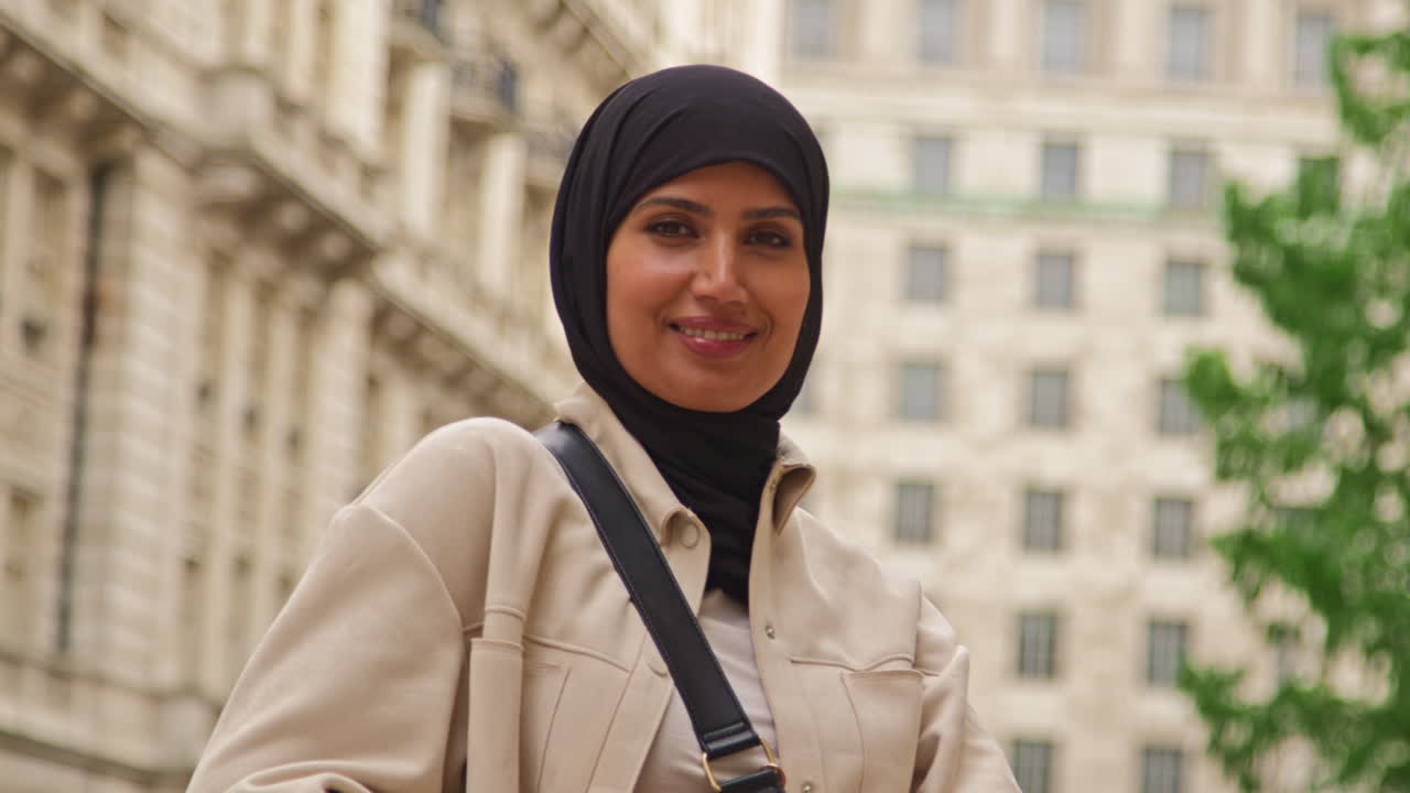 retrato de una mujer de negocios musulmana sonriente con hijab y traje de negocios moderno de pie y cruzando los brazos fuera de los edificios de oficinas de la ciudad