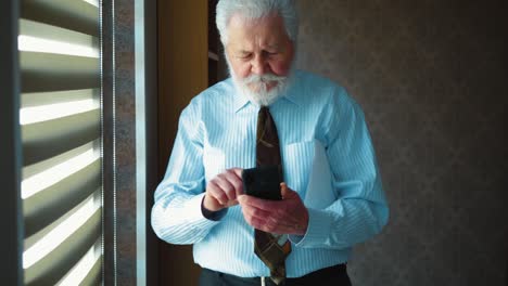 successful elderly businessman using smart phone standing in office. corporate messaging concept