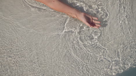 Playful-little-child-moves-hand-lying-on-shallow-beach-edge