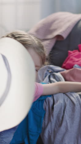 niña pone elegante sombrero de paja en la maleta con ropa en el sofá de primer plano. niño ayuda a reunir artículos para las vacaciones. accesorios para el descanso en la playa