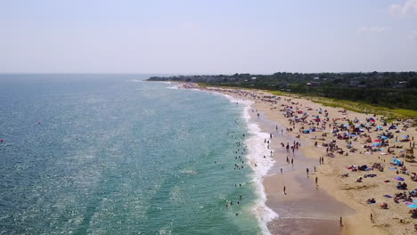 drone panning up shot of ocean with waves breaking and vacationers at the beach