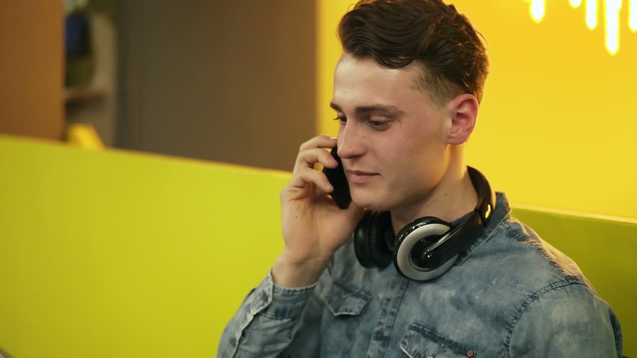 Attractive handsome man in his 20's laughing and smiling while chatting with someone on the phone. Indoors footage.