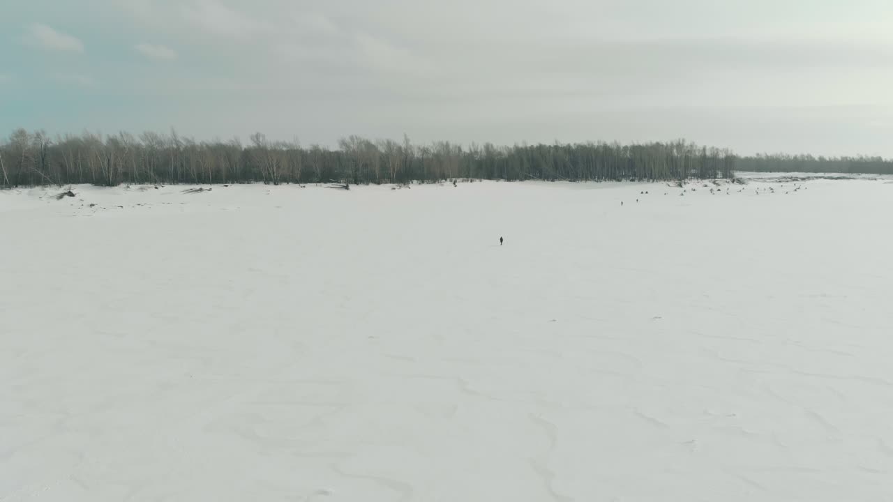 흐릿한 사람 실루엣이 얼어붙은 강 위의 모습을 따라 걷는다