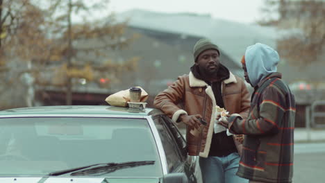 african american men having eating takeaway food and talking by car