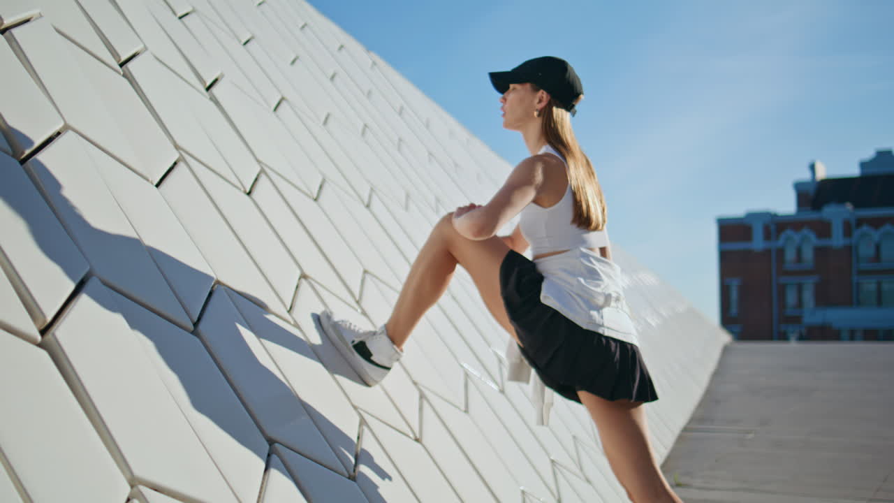Fit lady warming legs muscles leaning on geometric urban wall. Sport woman