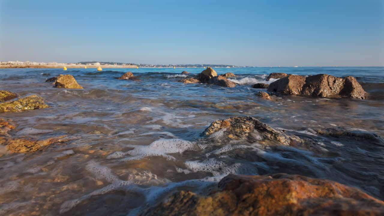 Vista di onde marine che lambiscono dolcemente la costa rocciosa sotto un cielo azzurro limpido