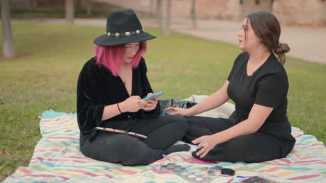 two women having a conversation and doing makeup in a park