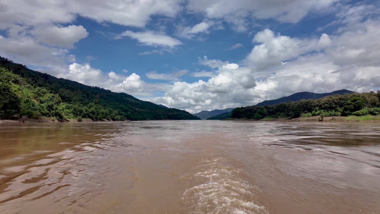 Muddy Mekong river flowing between lush green mountains under a cloudy sky in Laos