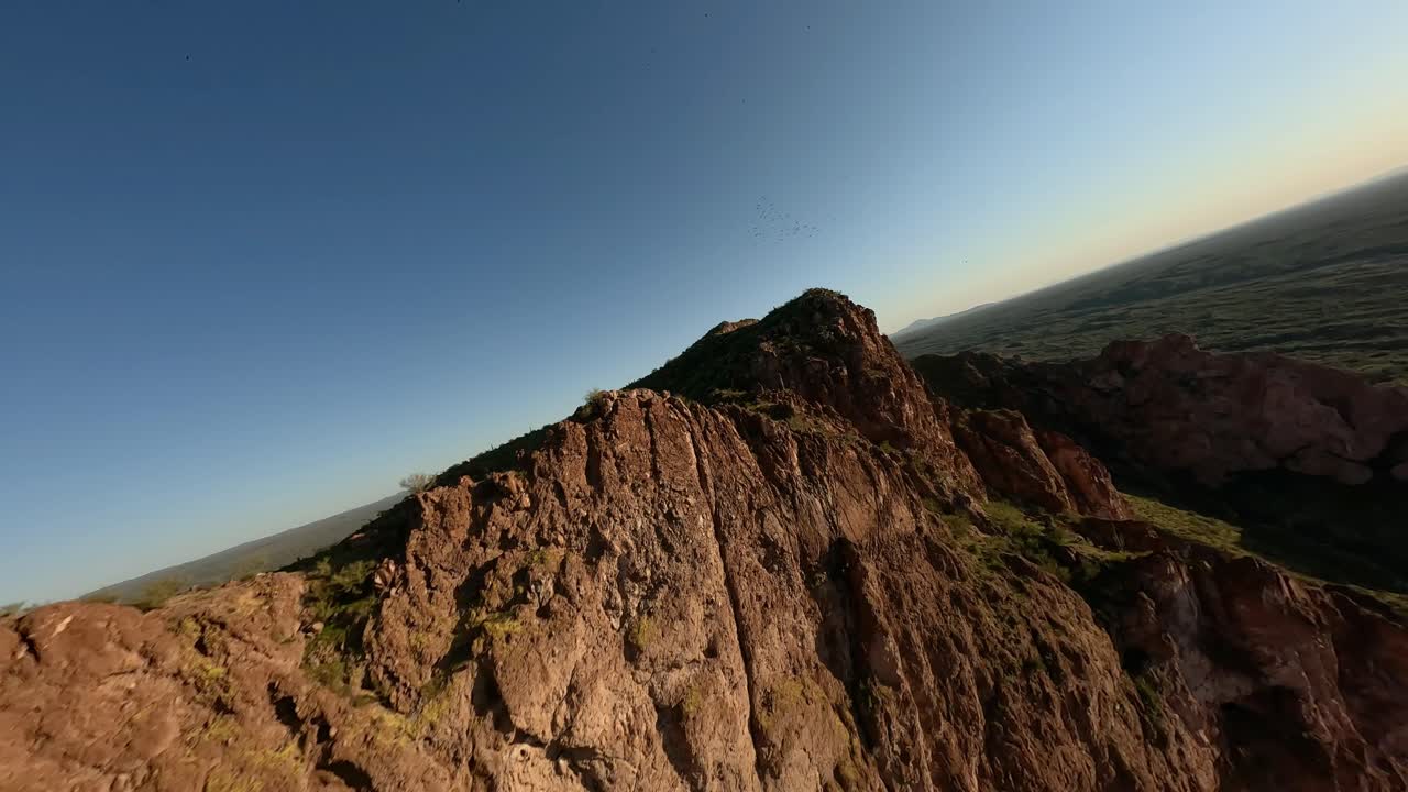 fpv aéreo volando sobre acantilados de piedra arenisca en el desierto de arizona con bandadas de aves volando más allá durante el atardecer