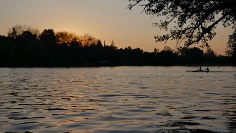 Slow-motion,-silhouette-of-two-men-paddling-canoes-in-dam-at-sunset,-golden-hour