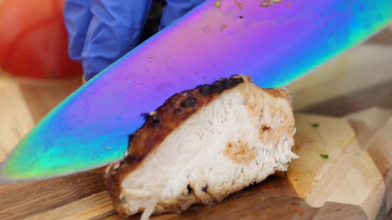 Chopping thin slices of roasted pork with a big knife while wearing rubber gloves, closeup on cutting board
