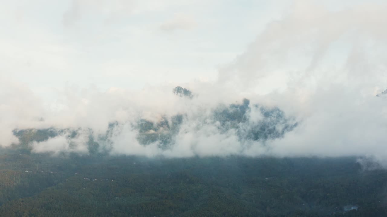 abriendo toma aérea de drones de una montaña cubierta de bosque verde, volando a través de nubes ligeras y tenues