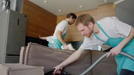 confident group of three cleaners in a white t-shirt and blue aprons are cleaning a modern kitchen in an apartment on call. the cleaning company sends a group of cleaners to clean the apartment