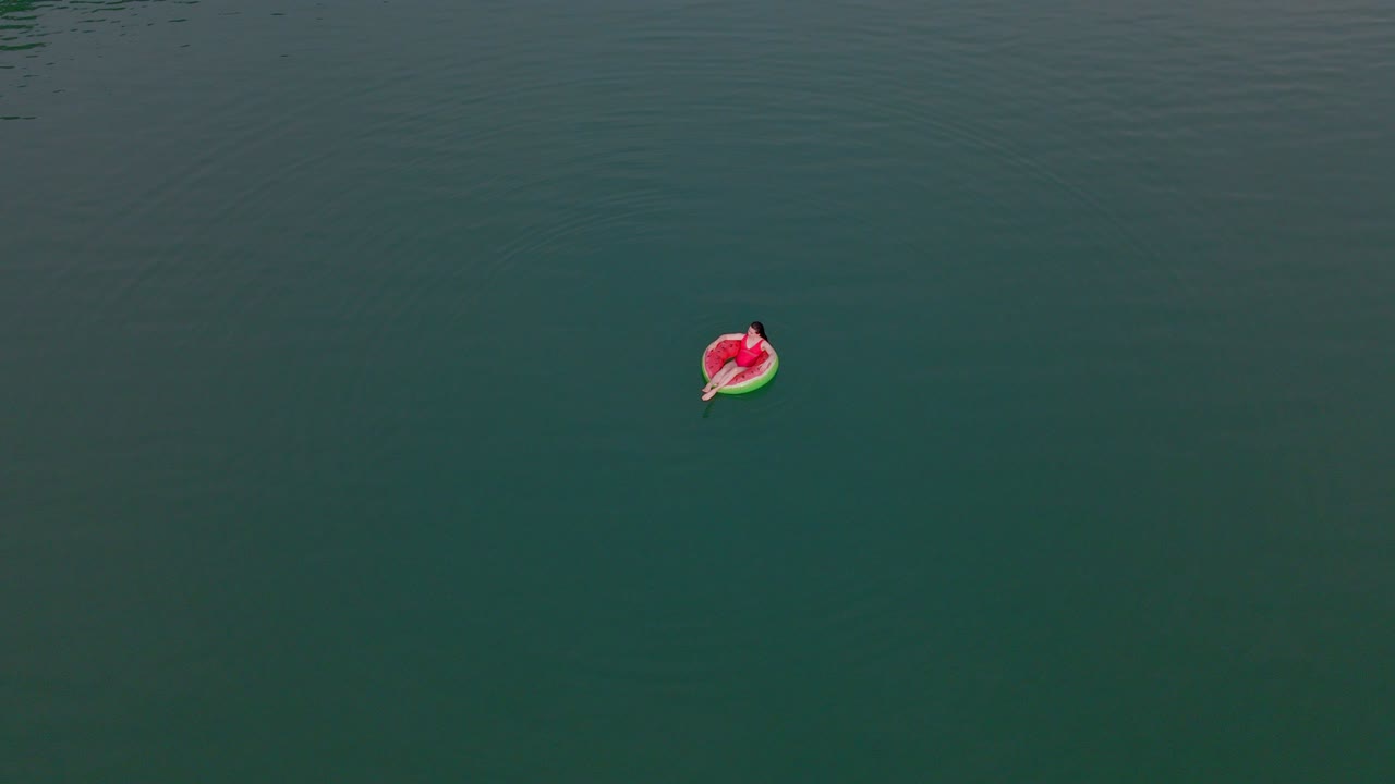 overhead top view of woman swimming with watermelon swimming circle in blue water