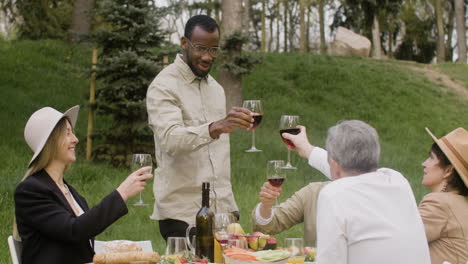 man standing in front of a table toasting with his friends at an outdoor party in the park