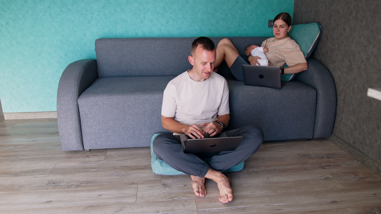 First time parents working remote and care about newborn. Caucasian couple work on their laptops.