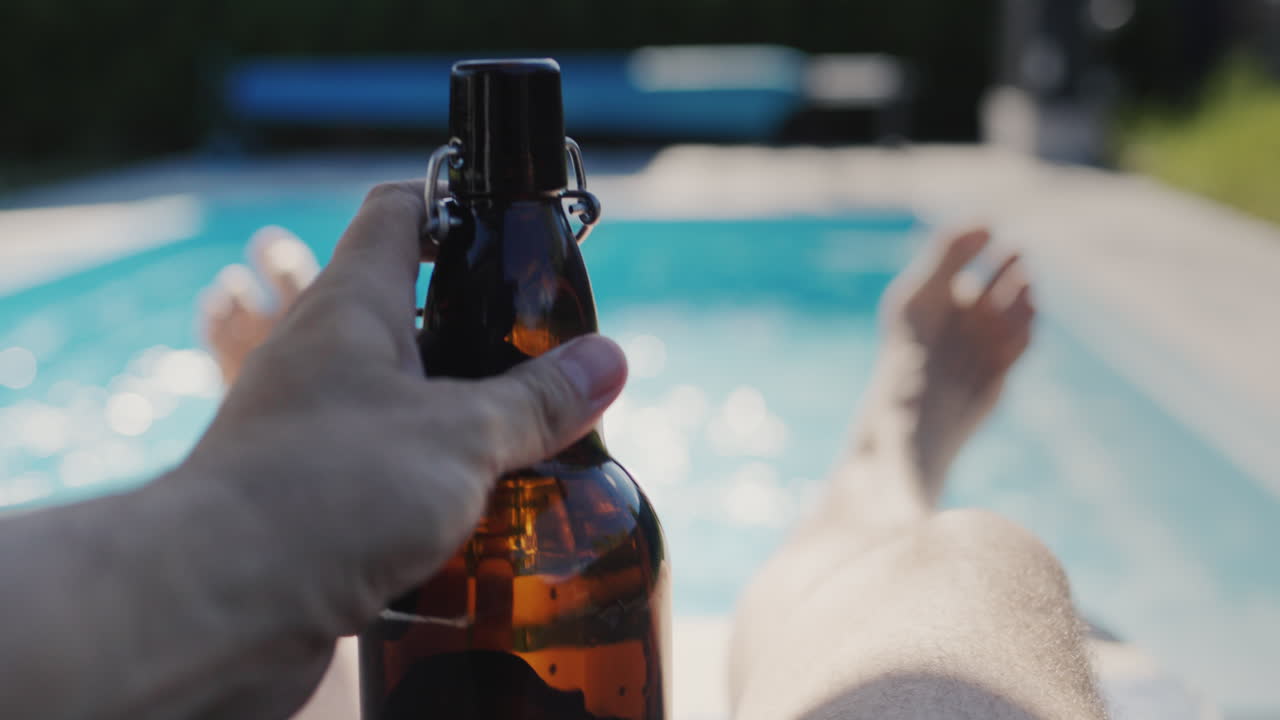 un hombre con una botella de cerveza se relaja cerca de su piscina en un caluroso día de verano.