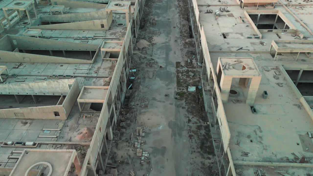 Ripresa aerea con drone di un cantiere edile incompiuto che mostra due edifici abbandonati in cemento divisi da una strada vuota con detriti e impalcature. Ideale per progetti di degrado urbano, immobiliari o industriali.