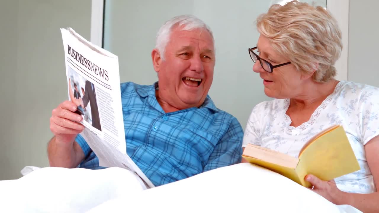 una pareja de ancianos sonrientes leyendo el periódico