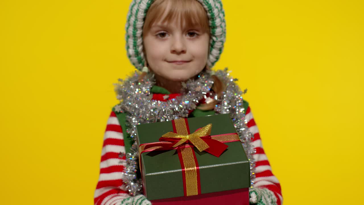 Dívka jako vánoční skřítek, pomocník Santa Clause, dává dárkovou krabici do kamery. Šťastné novoroční svátky.
