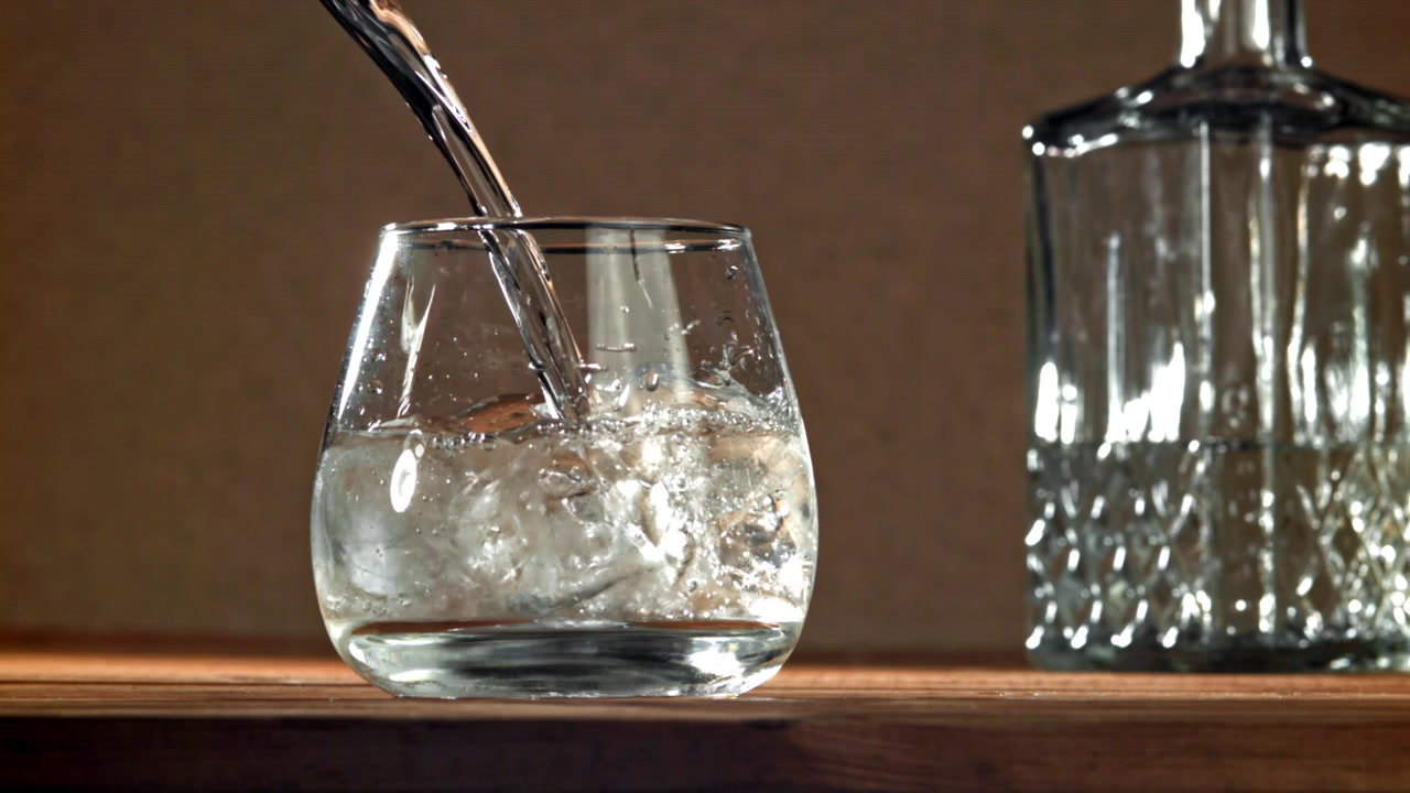 Klar væske hældes i et glas med isterninger