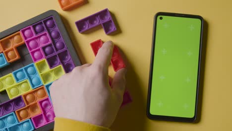 toma aérea de estudio de una persona jugando un rompecabezas de forma entrelazada con pantalla verde teléfono móvil sobre fondo amarillo