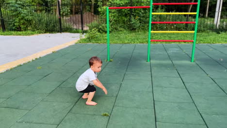 baby boy running by the playground, trips and falls down. kid stands up and goes to the ladder.