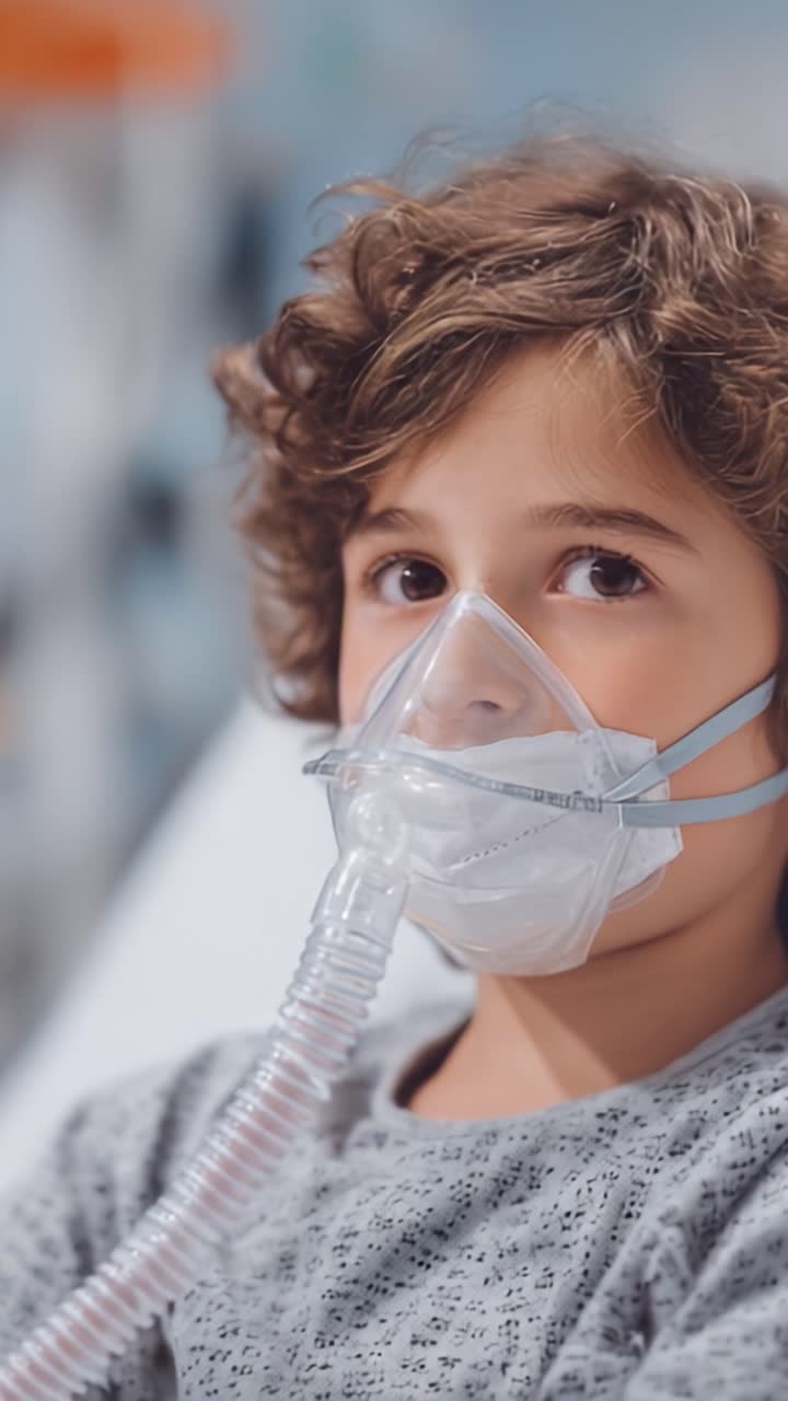 Un giovane ragazzo che indossa una maschera protettiva e un apparecchio respiratorio mentre riceve cure in una struttura medica, mostrando la sua calma nonostante la sfida per la salute