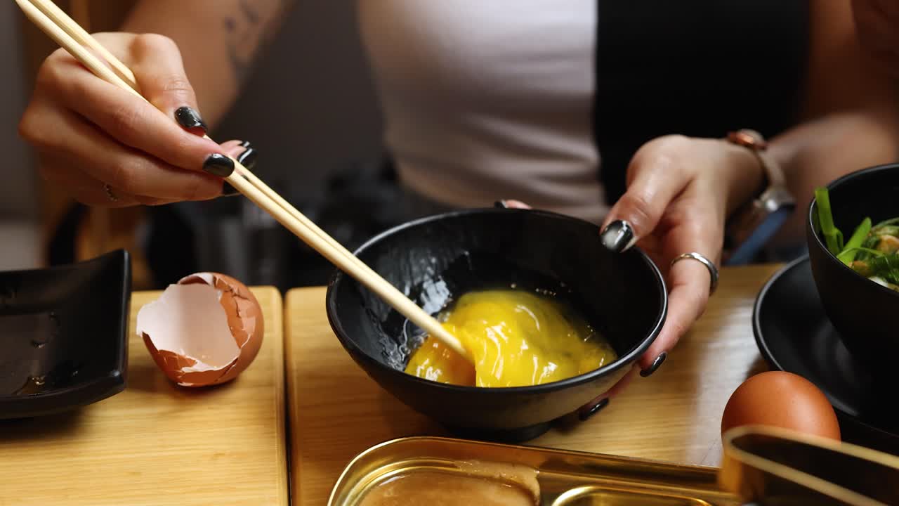 Close-up of hands stirring raw egg in bowl, warm lighting, shallow depth, Asian cuisine setting