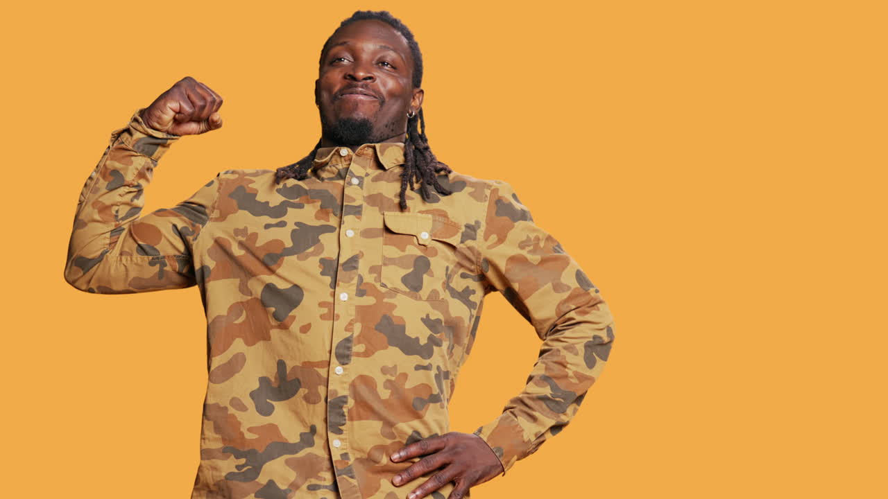 운동력 있는 강인한 남자가 카메라 앞에서 팔꿈치 근육을 구부리고 있습니다.