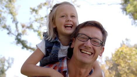 Dad-and-young-daughter-pulling-faces-in-a-park,-front-view