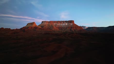 aerial establishing of moab iconic desert terrain, dramatic cliffs, valleys, and rugged landscapes with snow hidden in ridges at dusk
