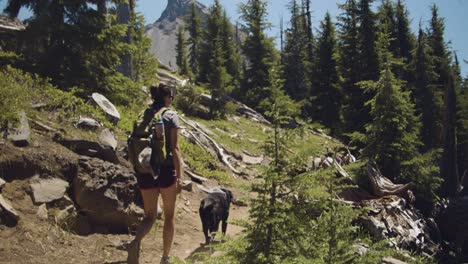 Girl-and-black-lab-hiking-on-dirt-trail-with-pointed-mountain-in-the-background