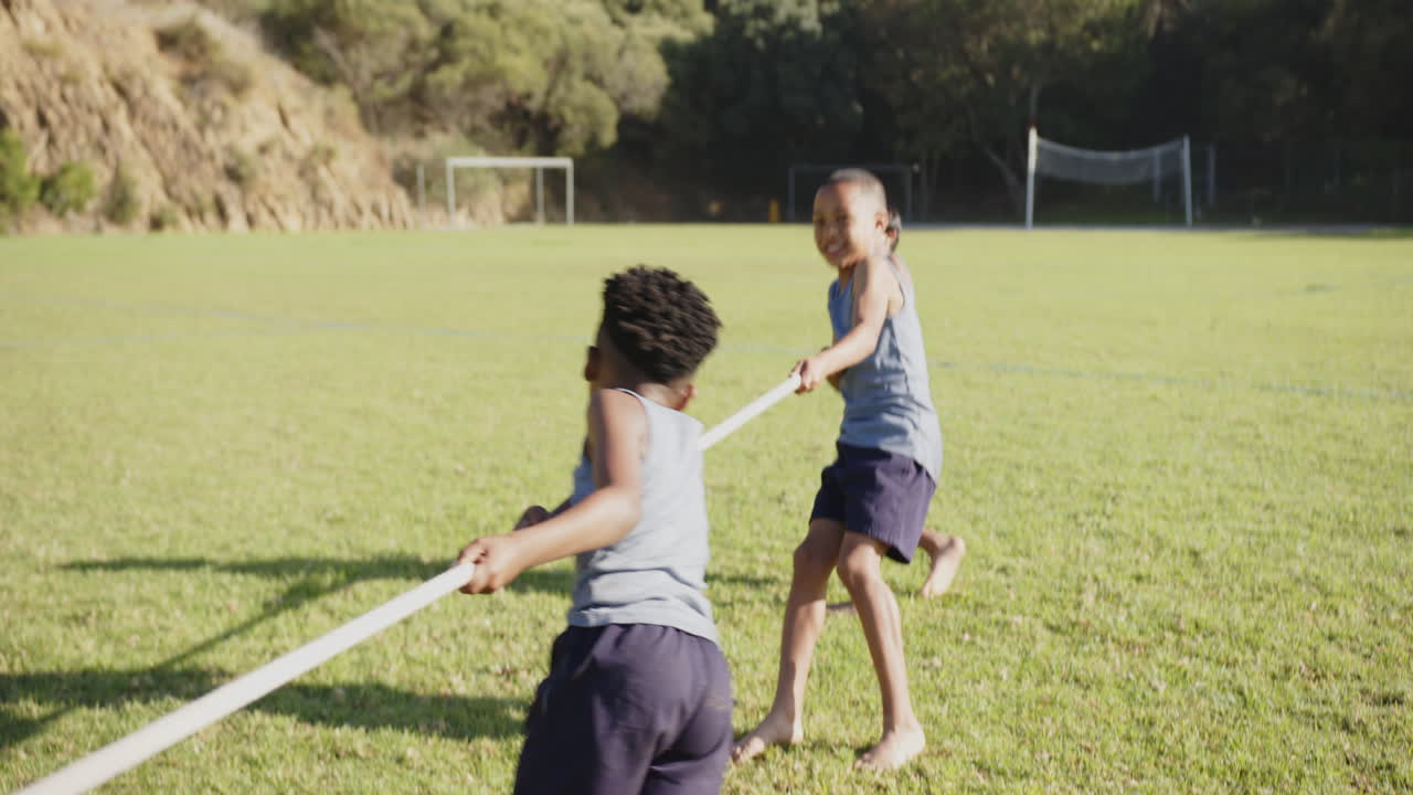 Playing tug-of-war, kids enjoying outdoor activity on school field with friends