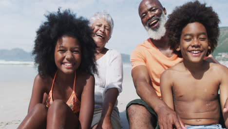 Retrato-De-Una-Pareja-Mayor-De-Raza-Mixta-Con-Nietos-Sentados-Y-Sonriendo-Sonriendo-En-La-Playa