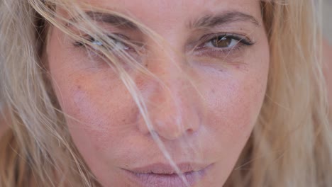 primer plano de una mujer rubia mirando a la cámara con una expresión melancólica mientras el viento sopla su cabello rubio