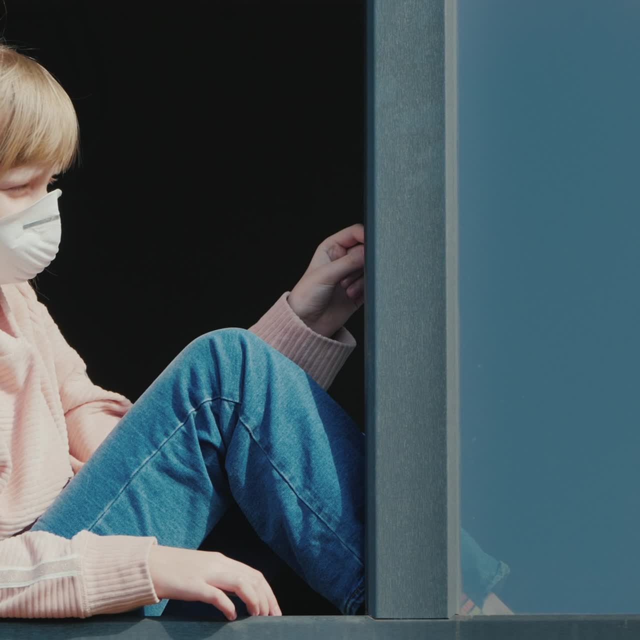 A Child In A Medical Mask Looks Out Of The Window
