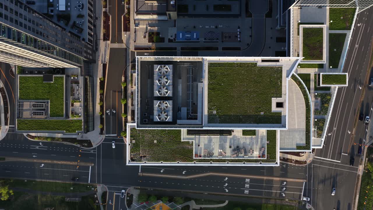 Modern downtown building with rooftop garden, cooling units and surrounding streets in an American city downtown. Warm sunlight showing sustainable urban design in USA. Aerial top down rising shot