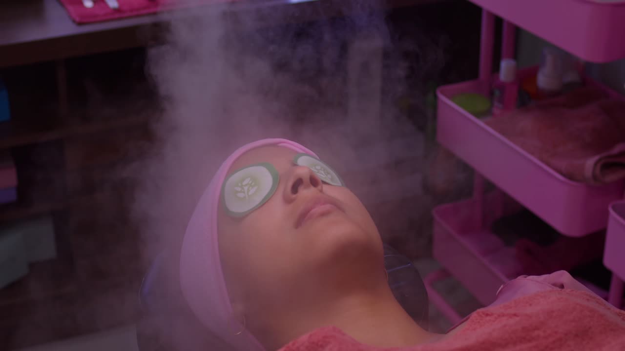 una chica se acuesta en una mesa en un spa con niebla soplando en su cara como un tratamiento de cuidado de la piel