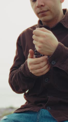 man holding a rosary in his hands during a prayer on the beach