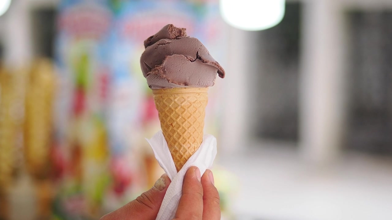 Mão segurando uma casquinha de sorvete de chocolate.